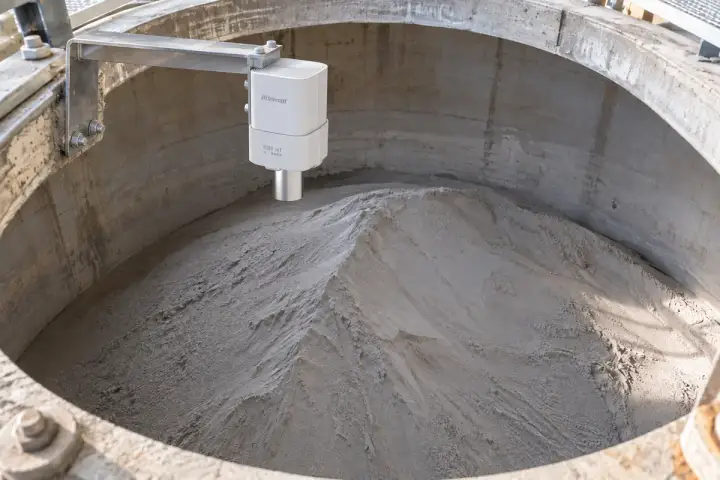Concept installation of a Hitelecom radar distance sensor on an upper silo-rim bracket facing a grey cement powder surface