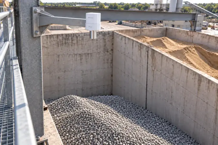 Concept installation of a Hitelecom radar distance sensor on a fixed steel-column arm over an aggregate pile beside a sand bunker