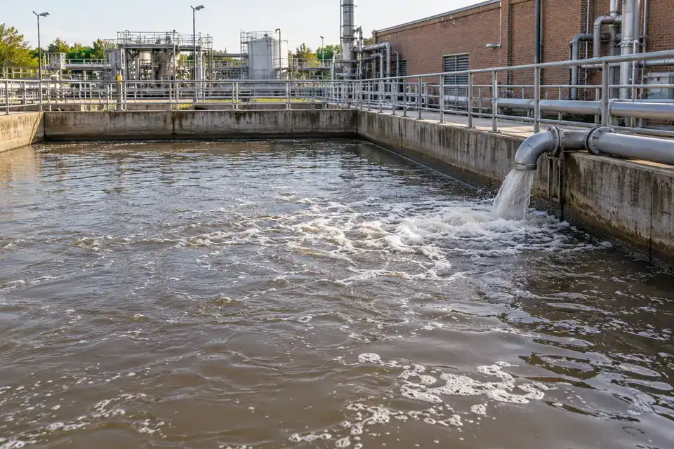 Industrial wastewater equalization tank with visible liquid, pipework and accessible treatment-plant walkway