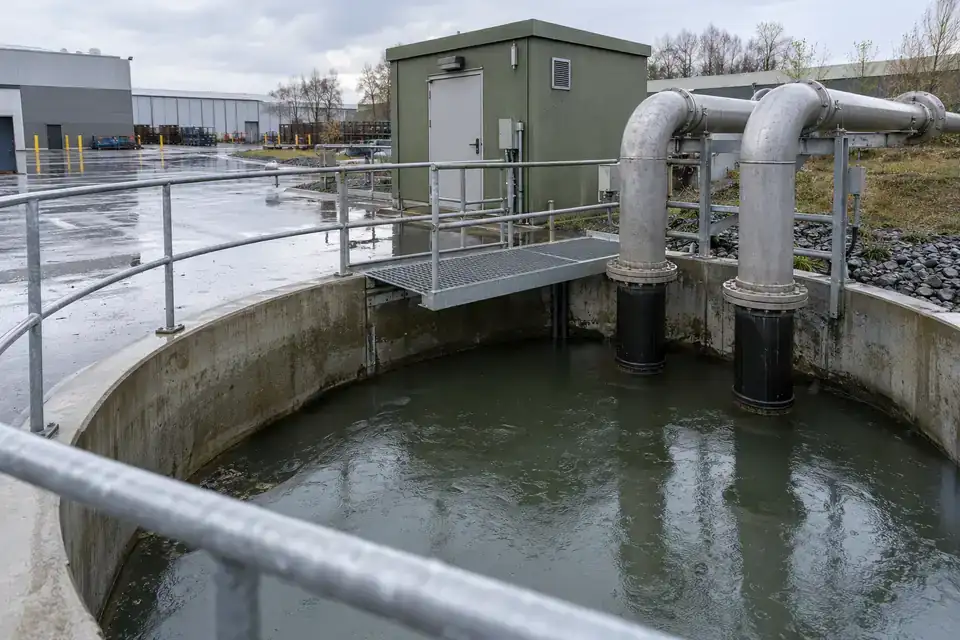 Outdoor factory stormwater lift station with a wet-well access area, drainage channels and industrial buildings