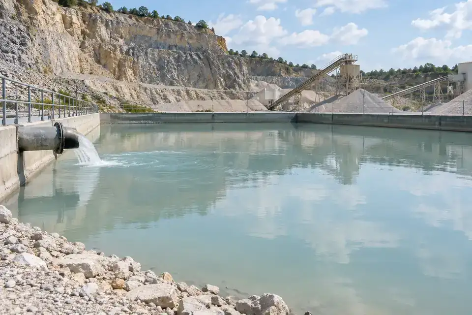 Quarry settling-water basin with defined water compartments, a transfer pipe and a dry service bank