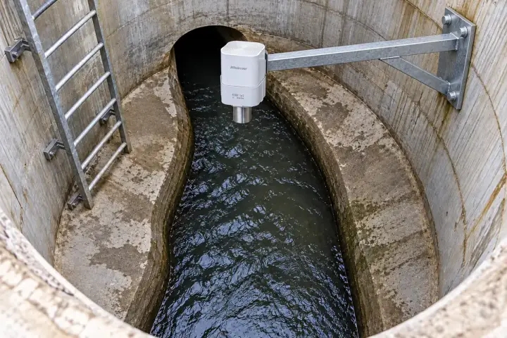 Concept installation of a Hitelecom radar sensor on a rigid upper-chamber bracket above the sewer flow-channel water surface.