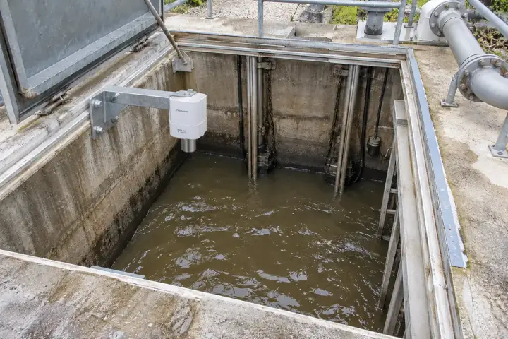 Concept installation of a Hitelecom radar sensor on an upper wet-well bracket above wastewater clear of pump risers.