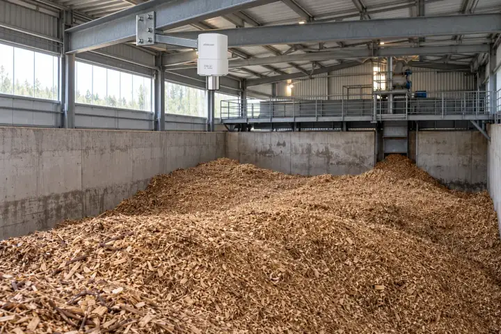 Hitelecom radar sensor on a rigid overhead bracket facing a woodchip surface inside a biomass bunker